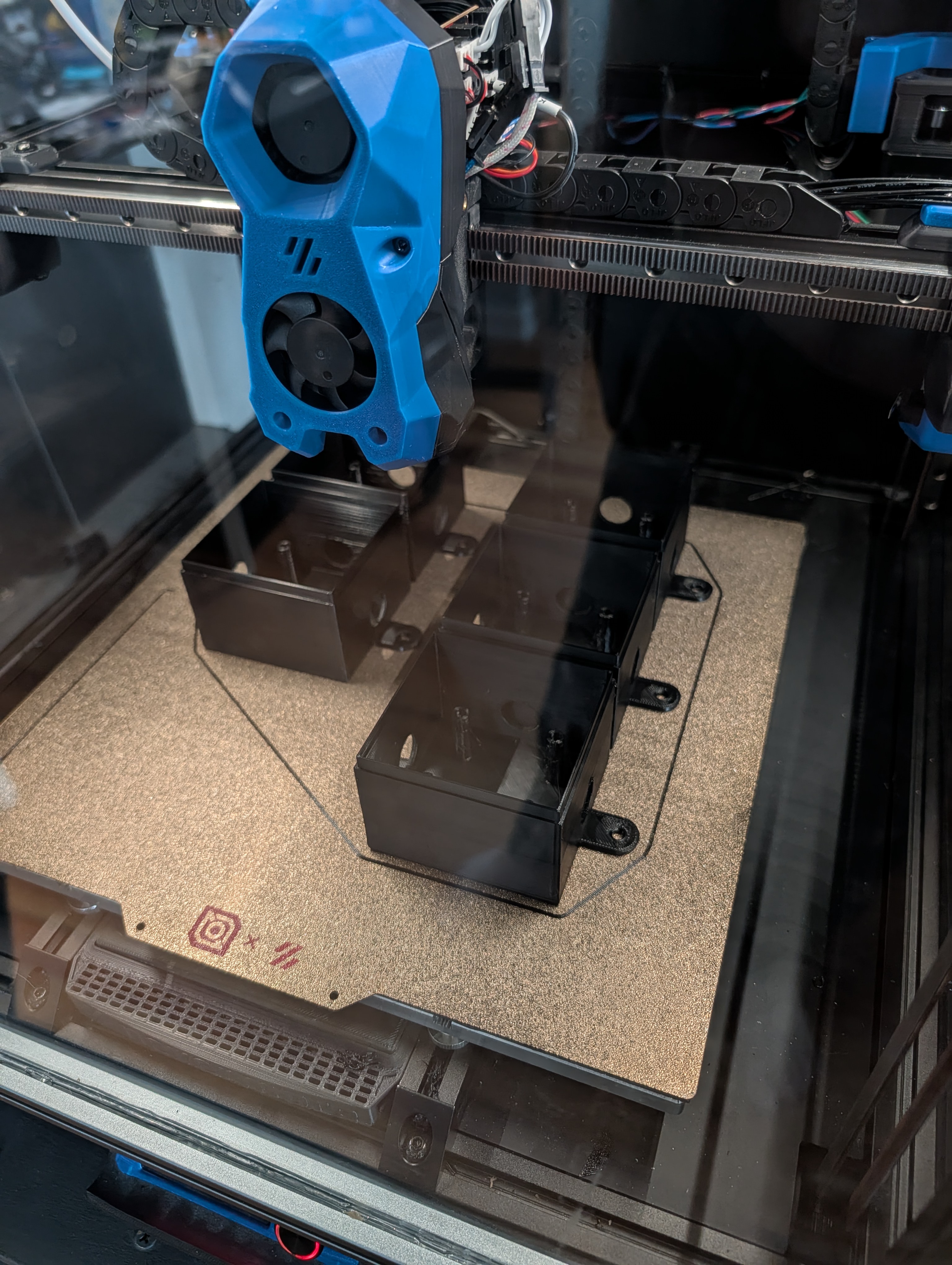 Five small plastic enclosures being printed on a 3D printer