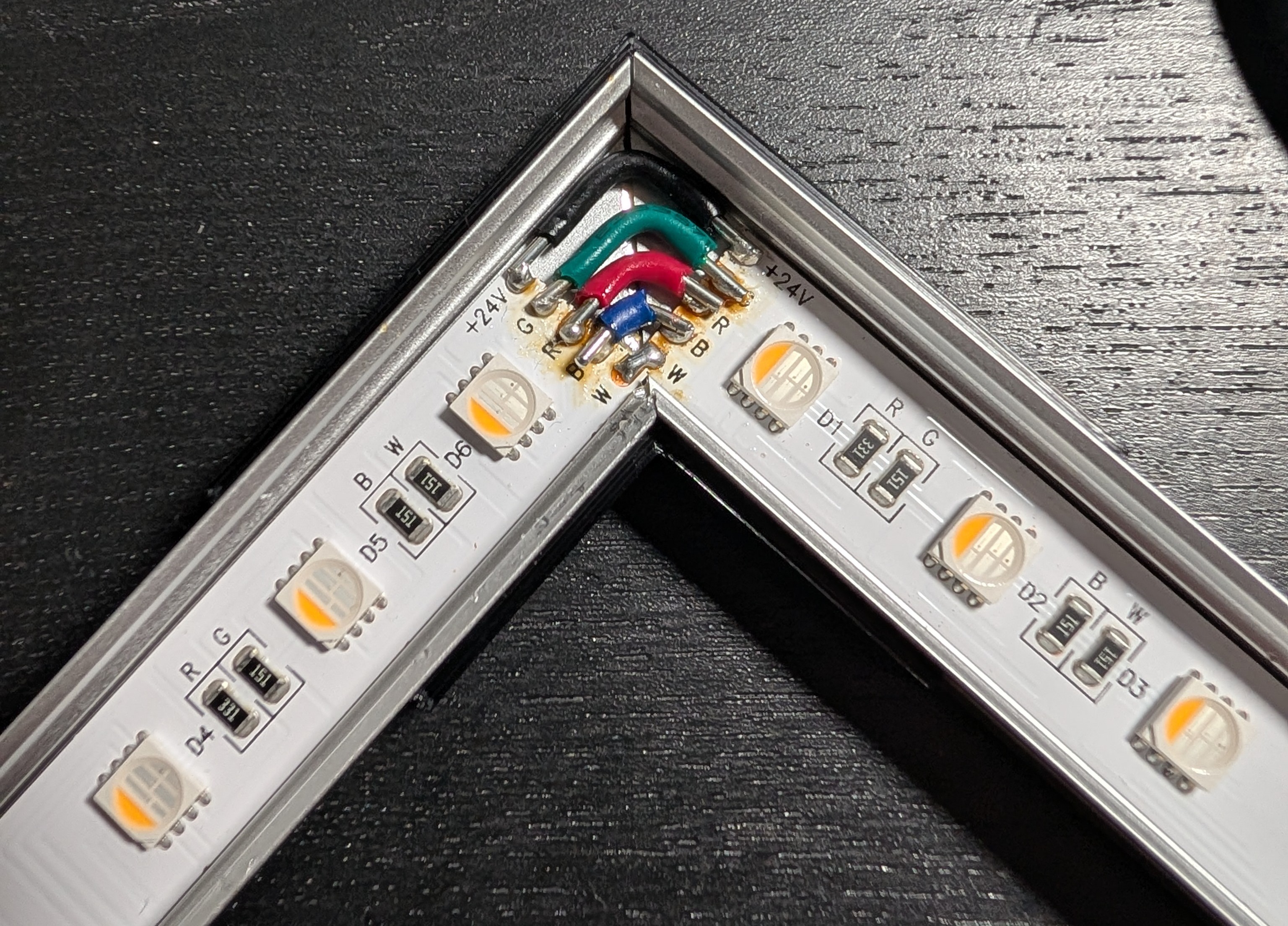 Closeup of a corner joint between two pieces of LED strip. There are four wires - black, green, red, and blue - turning the corner