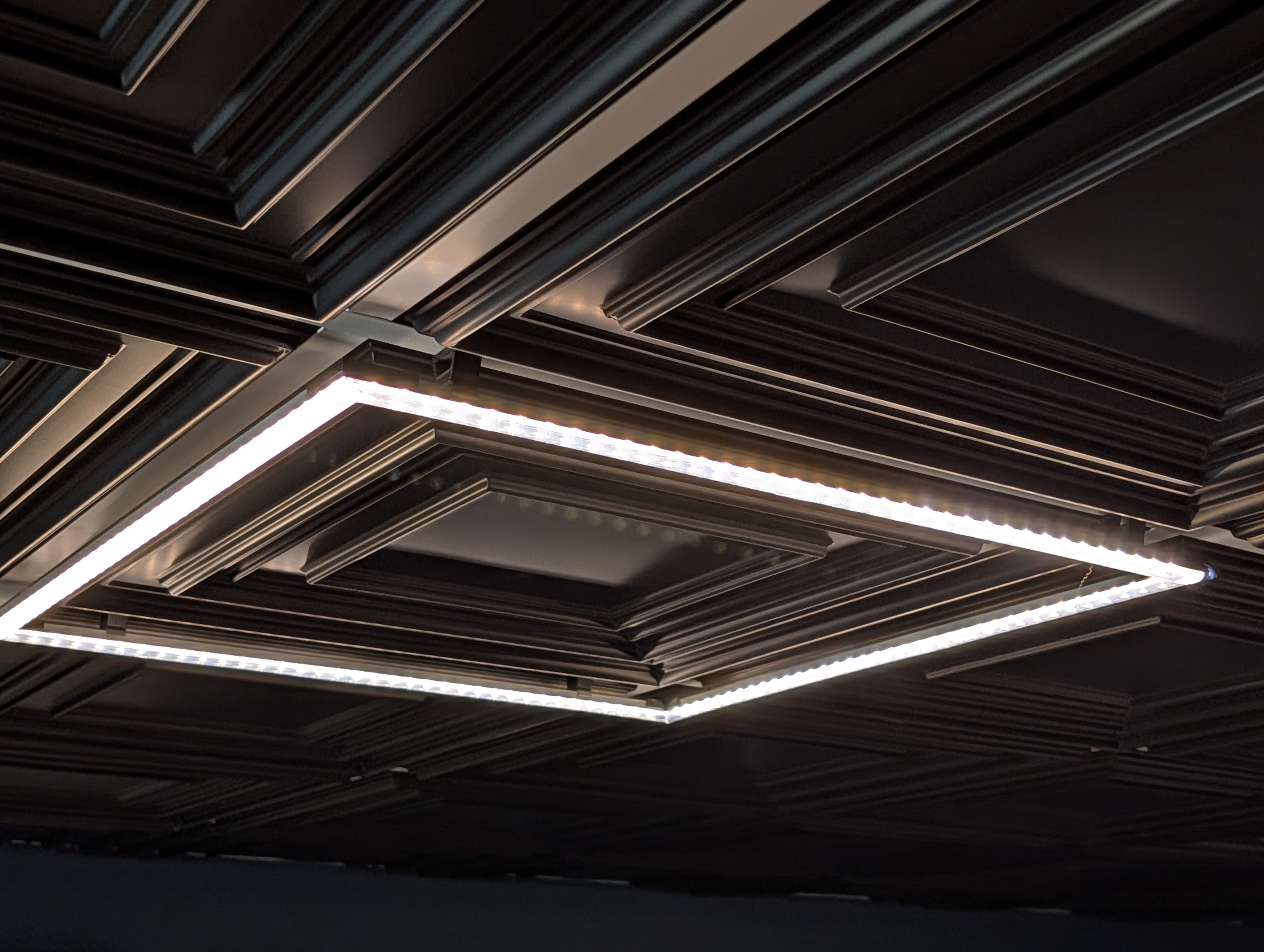 A square frame of LEDs attached to a ceiling grid, lit up white
